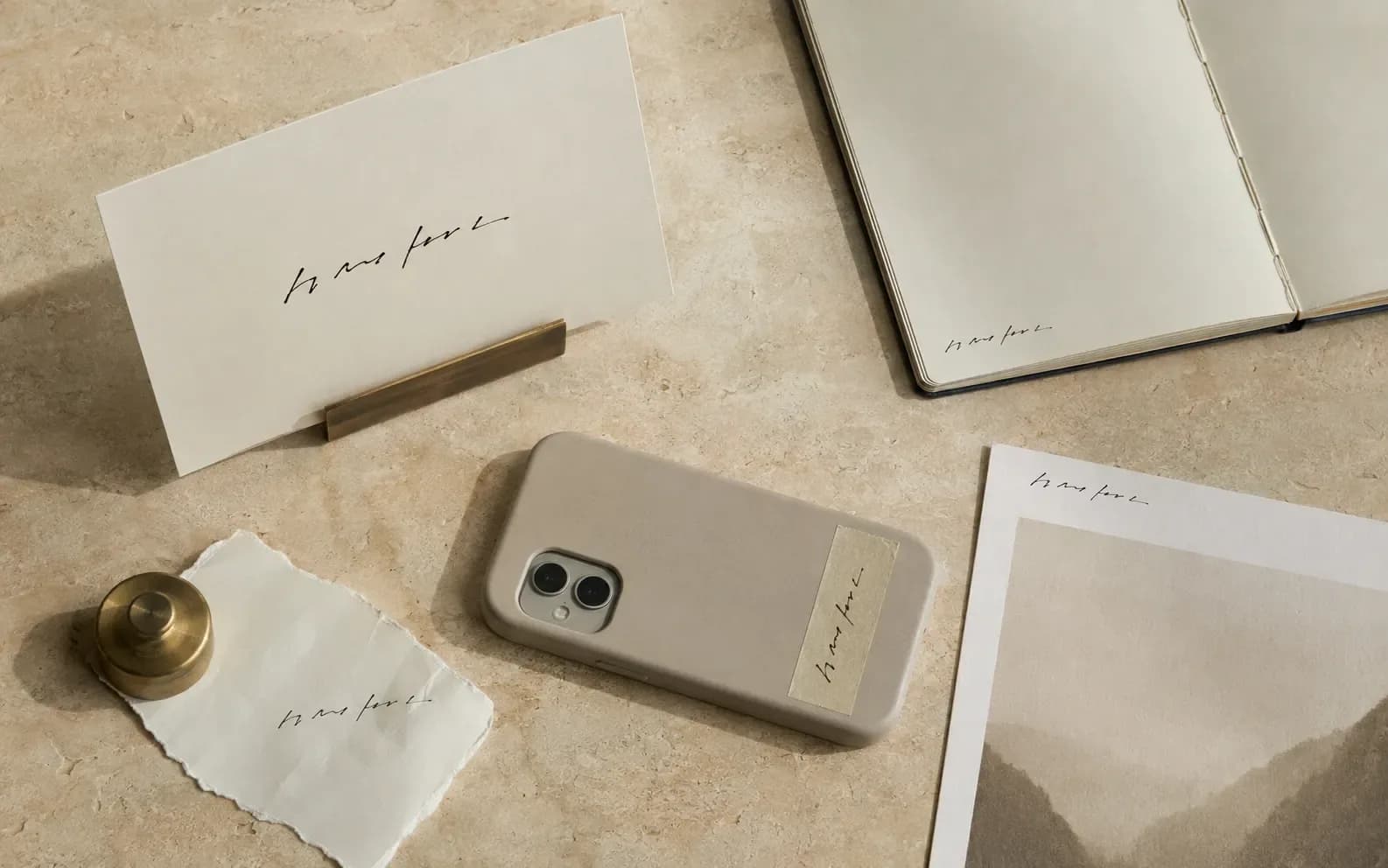The same short handwritten phrase in five places across one surface: on a card in a stand, in a notebook, on tape stuck to a phone, on a scrap under a brass weight, and on the back of a print.