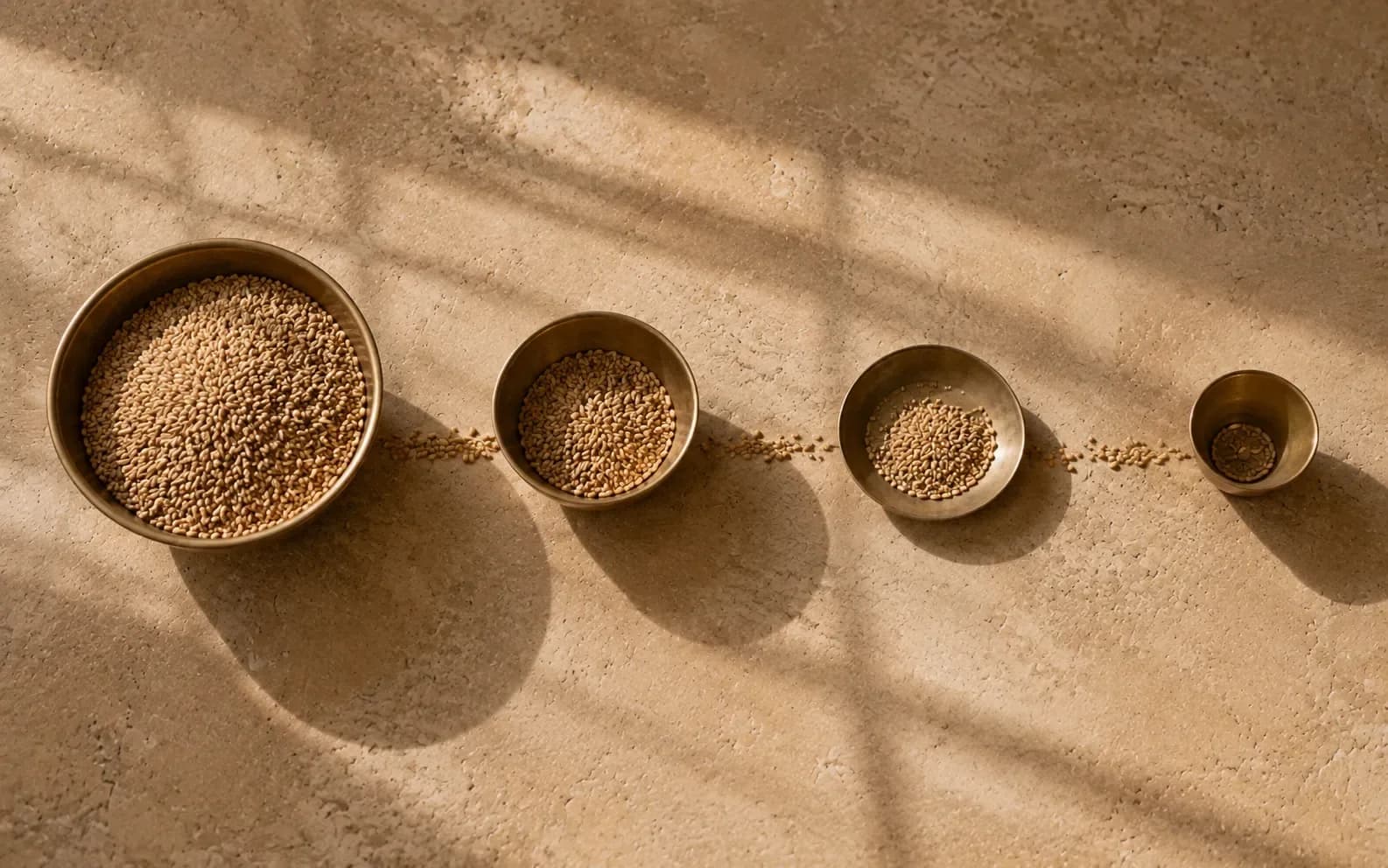 The same grain measured out at four points along a line, each vessel holding visibly less than the one before, with a thin trail of spill running between them.