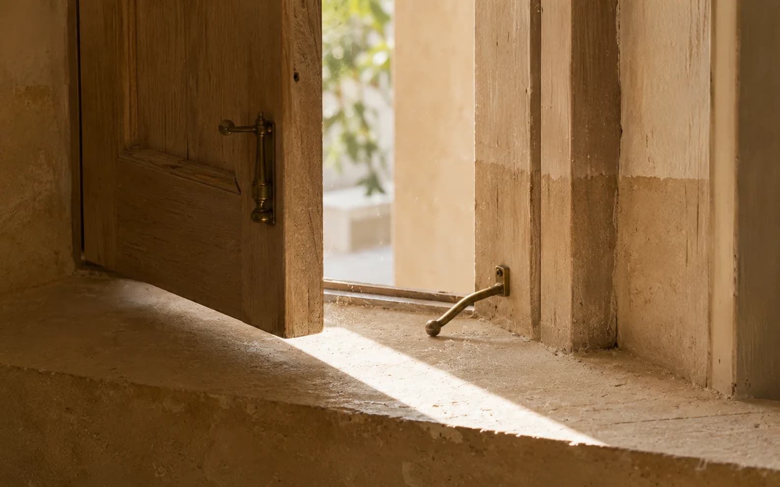 A wooden shutter standing open well past the paint line that shows where it used to stop, letting a wide band of daylight across a stone sill.