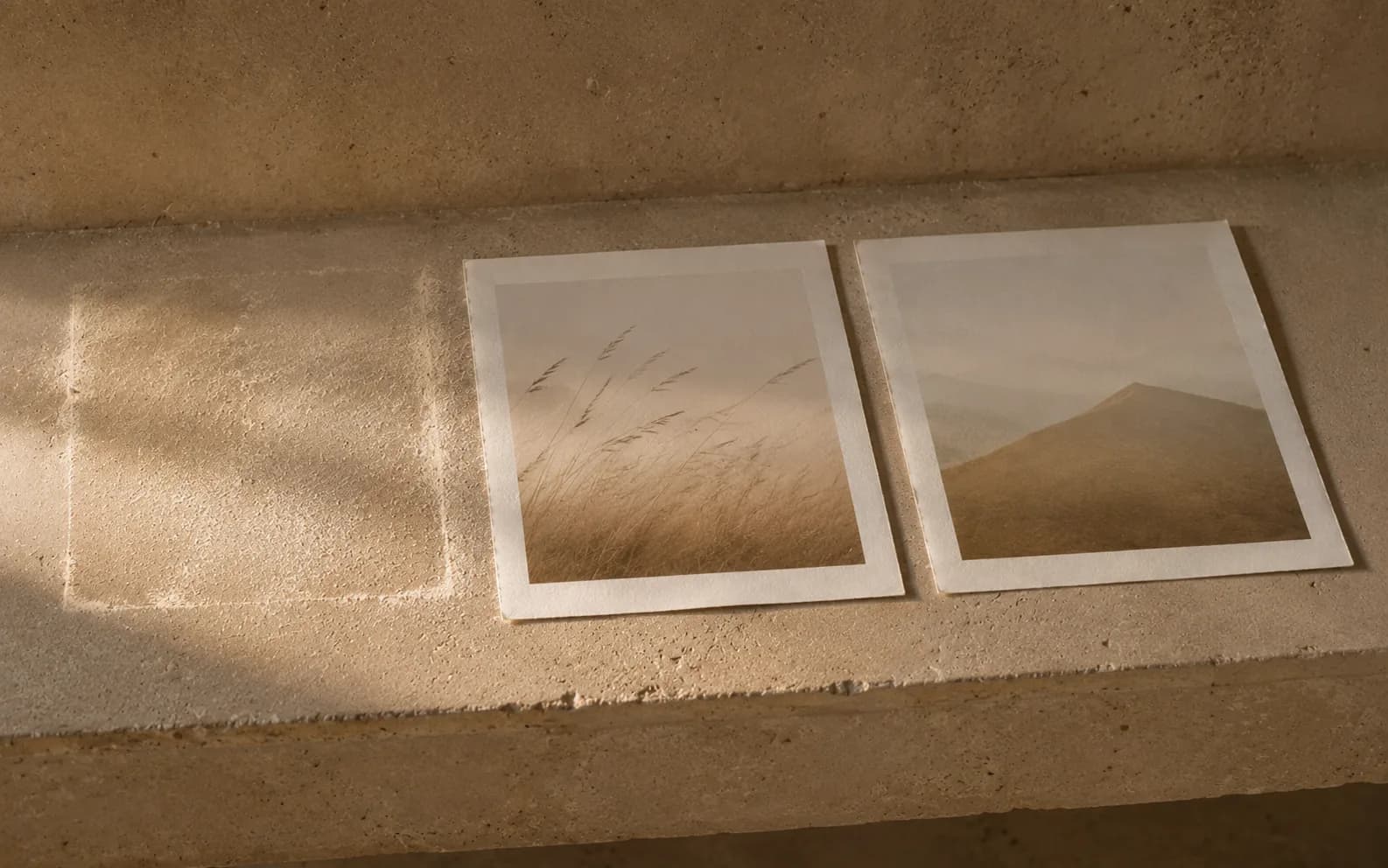 Two finished prints sitting untouched on a stone shelf, dust settled around them and a cleaner rectangle where something else was taken away.