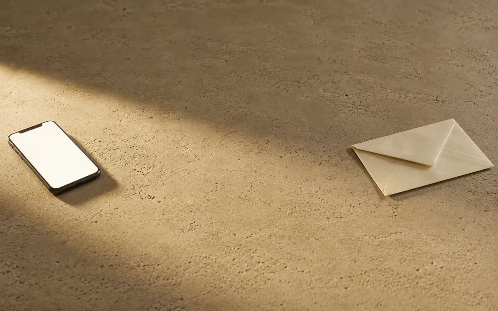 A phone lying face up at one side of a stone surface and a sealed cream envelope at the other, with nothing at all between them.