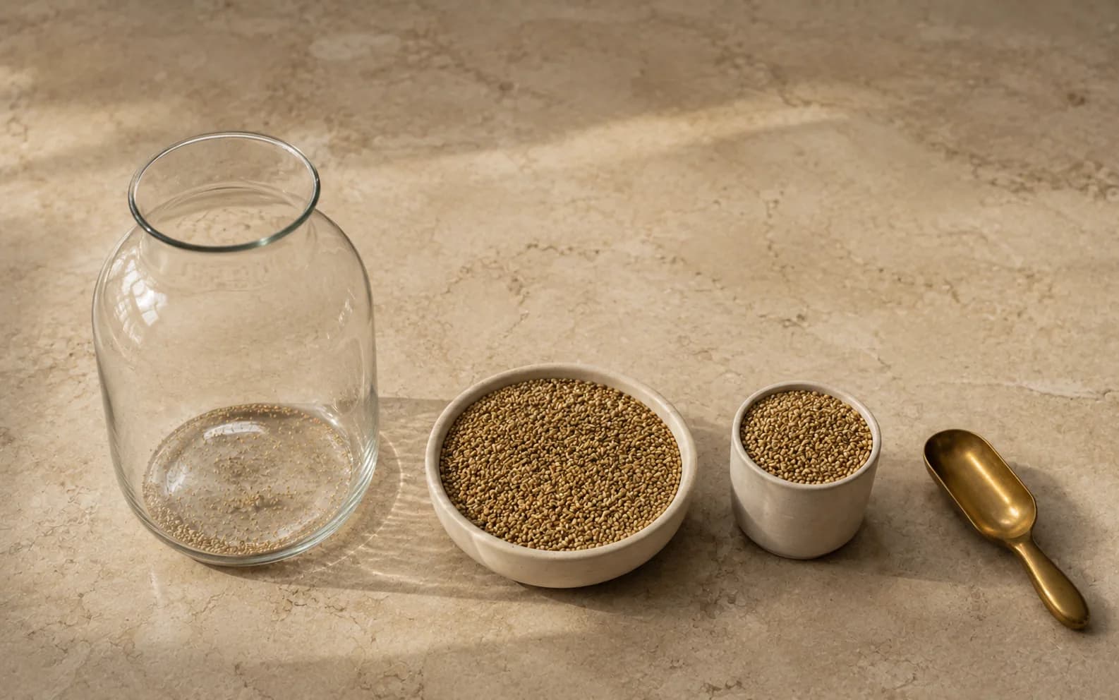 A tall glass jar standing almost empty beside two smaller, plainer vessels filled to the brim with the same grain.