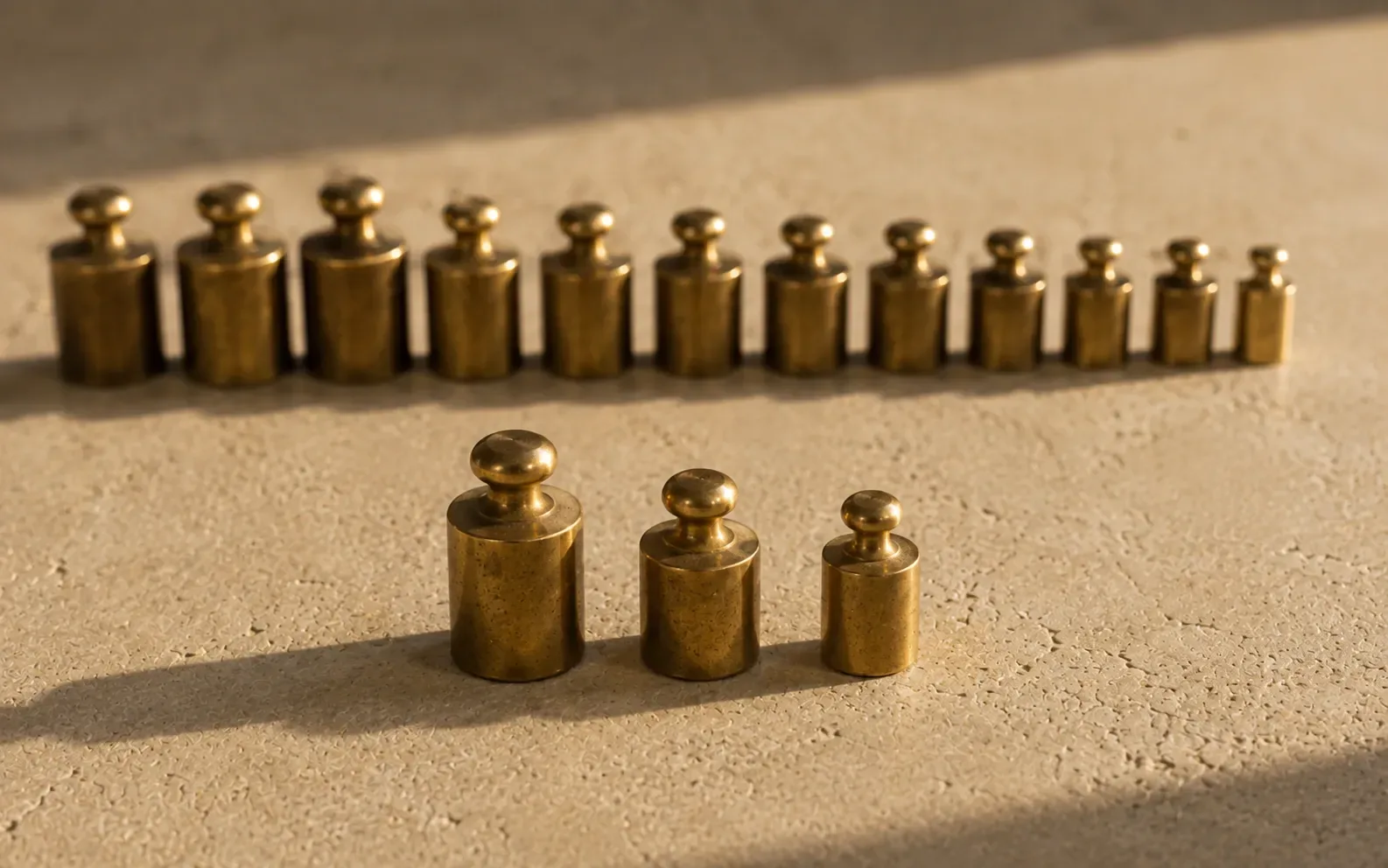 A long row of small brass weights on stone with exactly three of them picked out and set forward in front of the rest.